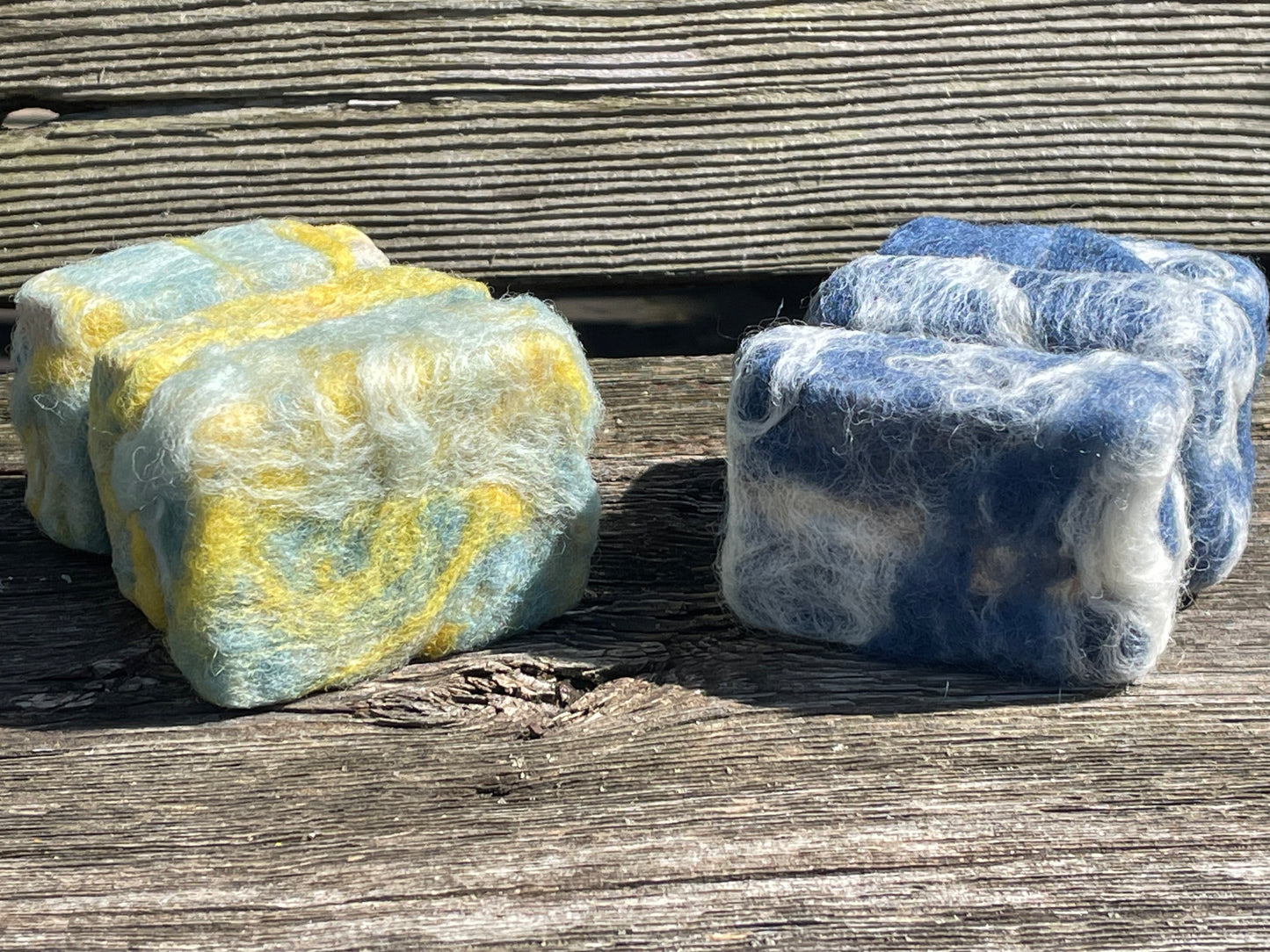 Six blocks of soap, three yellow and green, the three blue and white, on a wooden bench.